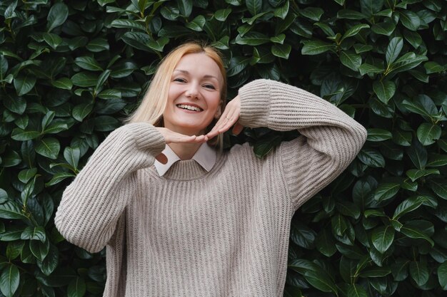 Friendly smiling attractive woman on background of green hedge Happy confident woman in front of green leaves wall Concept of Joy Zen and Balance People Stability through mental health