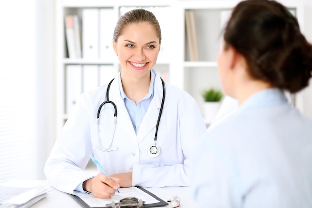 Friendly smiling doctor  and  patient sitting at the table. Very good news and high level medical service concept.