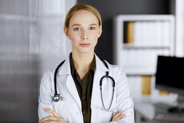 Friendly smiling female doctor standing in clinic. Portrait of friendly physician woman. Perfect medical service in hospital. Medicine concept.