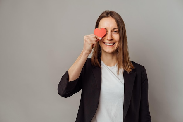 Friendly smiling woman wearing jacket covers one eye with a small red heart