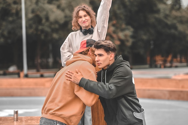 Friendly support. smiling girl raising hand looking at camera
and two friends hugging in park on fine day