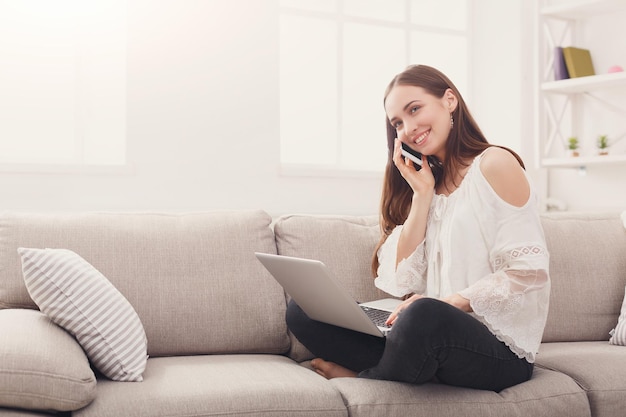 Friendly talk. Young woman chatting on mobile and surfing the Web on the laptop, copy space