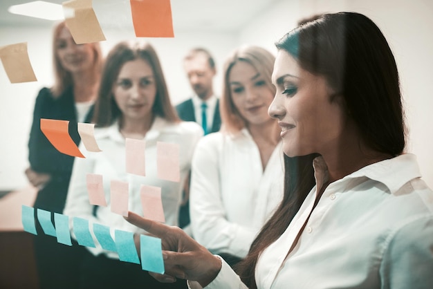 Friendly team business people brainstorming together looking on colorful stickers on office door win...