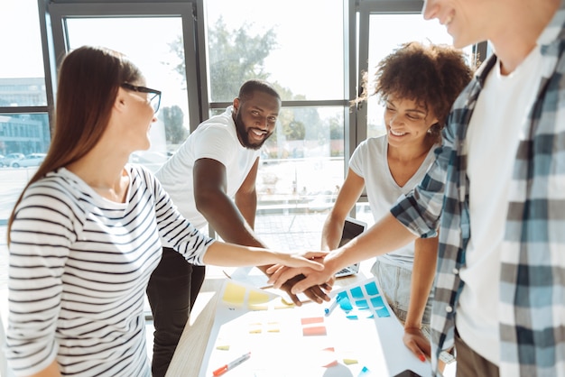 Friendly team. Positive young colleagues holding hands and enjoying friendly atmosphere while working together in the office