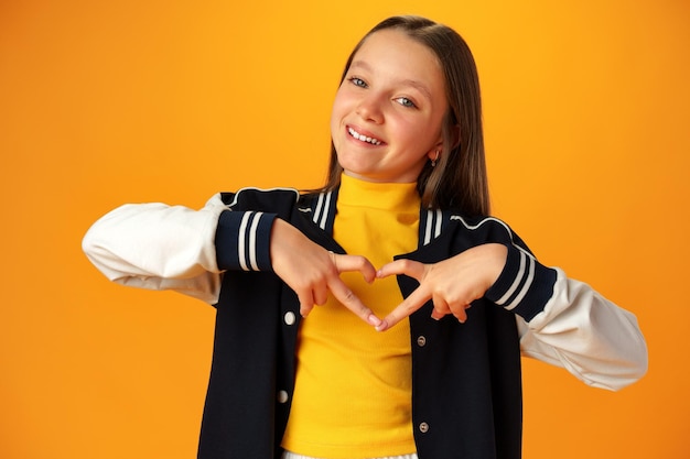 Friendly teen girl shows heart love gesture on yellow background