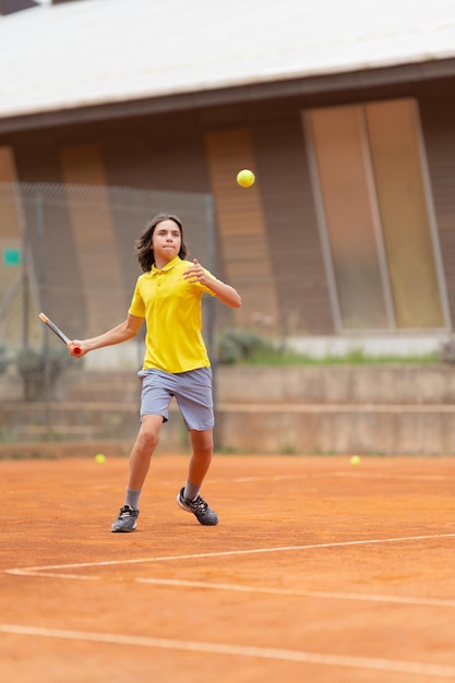 친선 테니스 경기 노란색 셔츠를 입은 소년이 공을 가져갑니다.