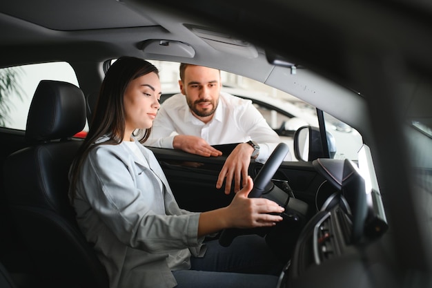 友好的な自動車ディーラーが若い女性に新しい車を見せている