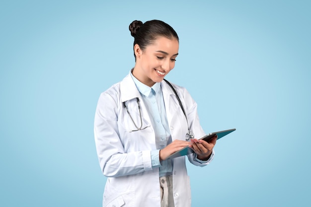 Friendly woman doctor in medical workwear holding digital tablet and consulting patients online over