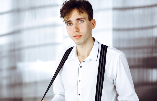 Photo friendly young businessman in white shirt is standing in modern office.