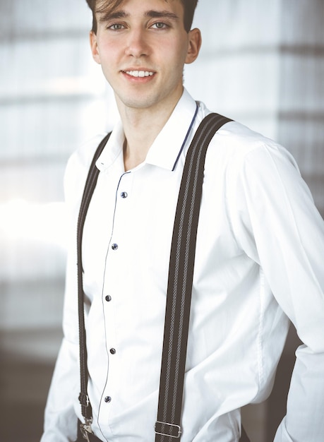 Friendly young businessman in white shirt is standing in modern office.