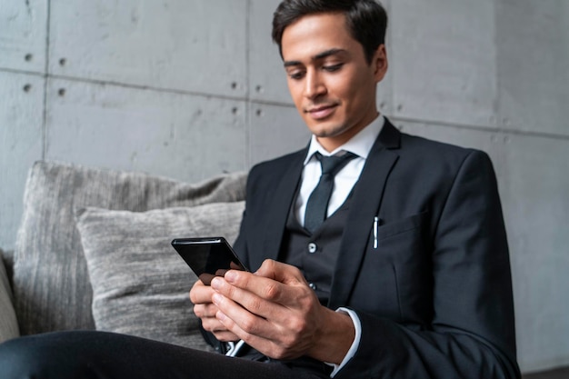 Friendly young businessman with phone in armchair