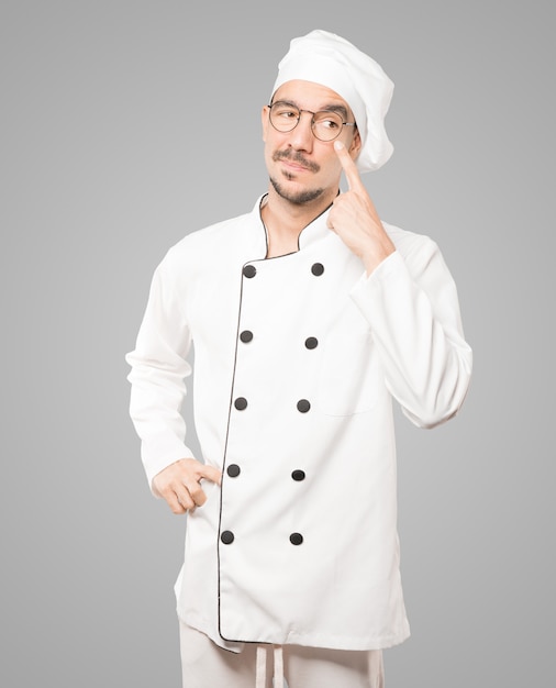 Friendly young chef making a gesture of being careful with his hand pointing at his eye