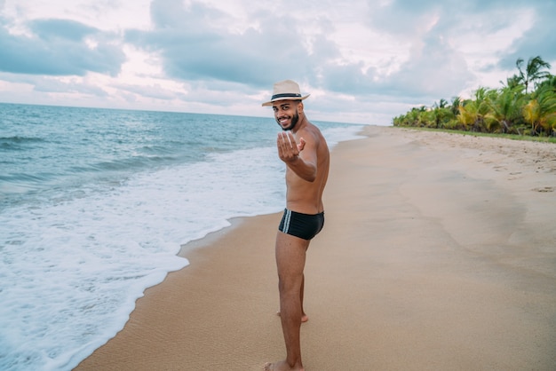 ブラジルに来るように誘うフレンドリーな若いラテンアメリカ人男性、自信を持って笑顔で手振りをし、前向きでフレンドリー