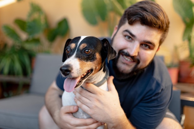 写真 彼のかわいい食料雑貨店の犬を両手で抱きしめ、カメラを見てフレンドリーな若い男