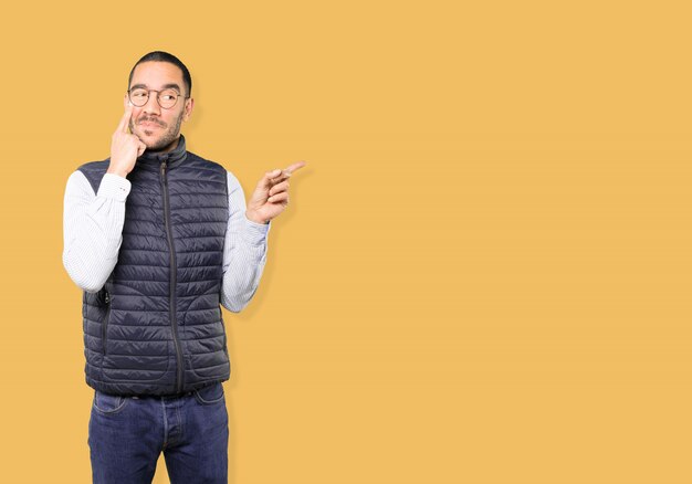 Friendly young man making a gesture of being careful with his hand pointing at his eye