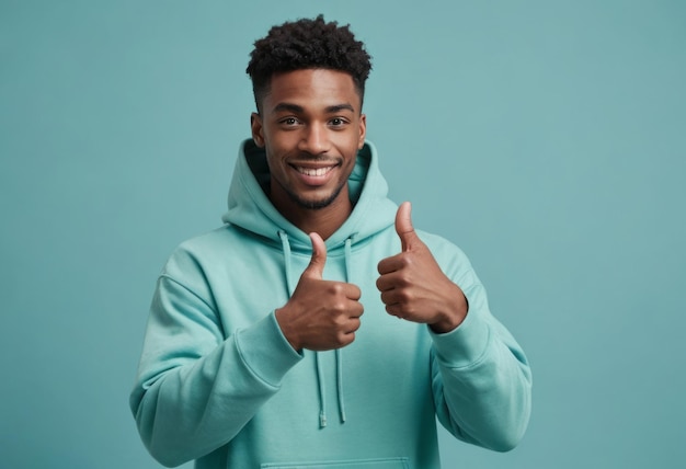 A friendly young man in a teal hoodie gives two thumbs up his smile infectious