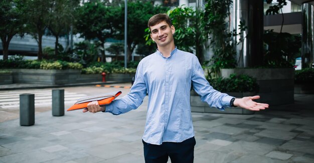 Friendly young student with folder smiling and stretching out arms