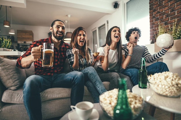 Friends are fans of sports games as football love spending their free time at home together. They are screaming and gesturing for a victory.