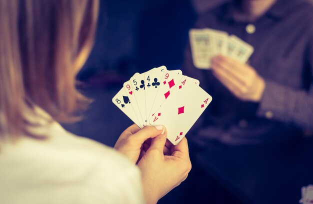 Friends are playing cards together at home woman is holding\
cards in her hands man in the blurry background