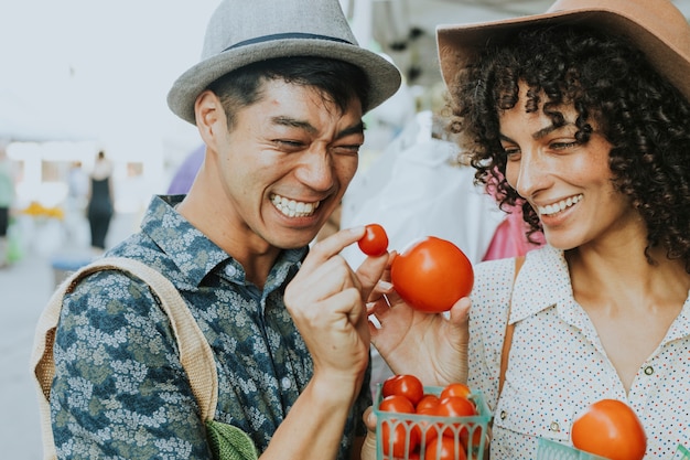 Amici che comprano i pomodori freschi ad un mercato degli agricoltori