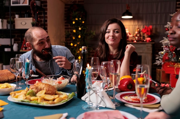 Friends celebrating christmas at festive dinner table, gathering at family home party. Man and woman eating xmas dishes in decorated beautiful place with warm candle light