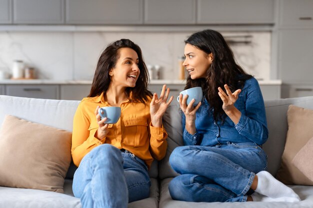 Photo friends chatting with coffee on couch at home