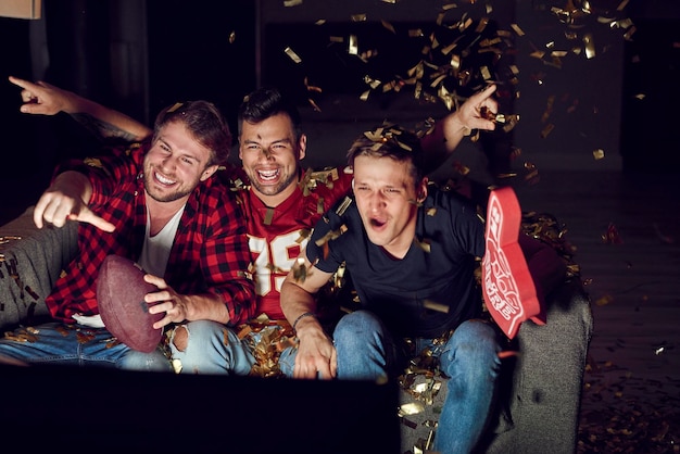 Photo friends cheering while looking at television set in living room