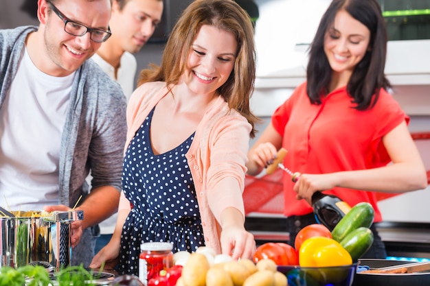 Amici che cucinano spaghetti e carne nella cucina domestica