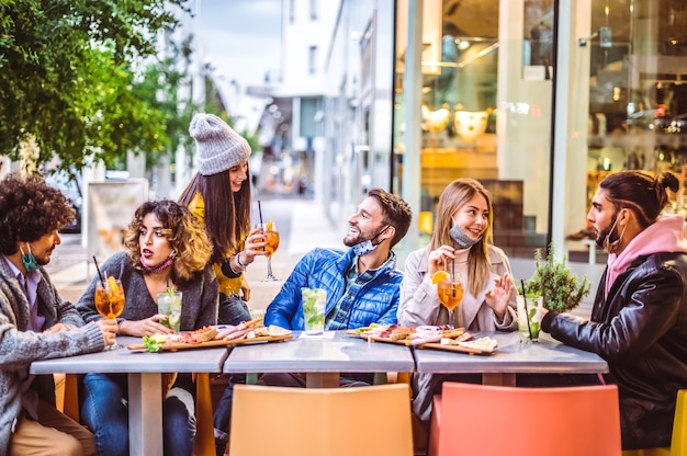 Фото Друзья пьют спритц и мохито в коктейль-баре с масками для лица - новая концепция нормальной дружбы, когда счастливые люди веселятся вместе, поджаривая напитки в ресторане