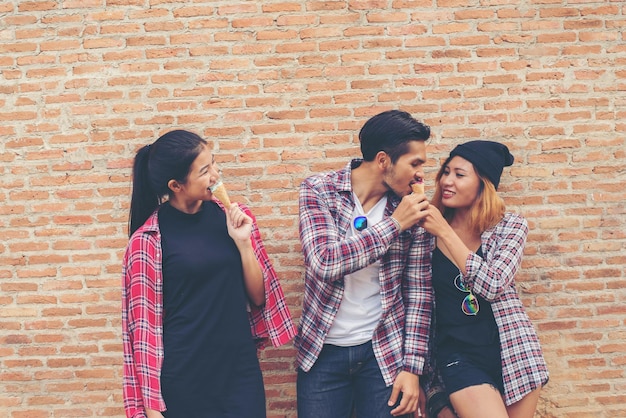 Photo friends eating ice creams while standing against brick wall