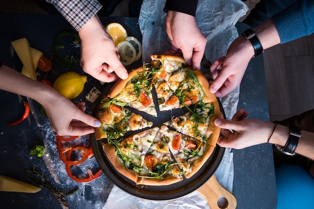 Friends eating pizza. People's hands grabbing a slice of pizza