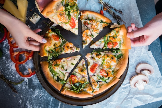 Friends eating pizza. People's hands grabbing a slice of pizza