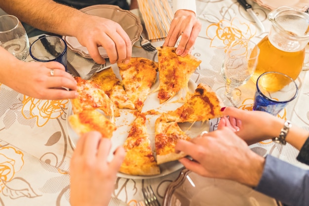 Friends eating pizza together, hands grabbing pieces