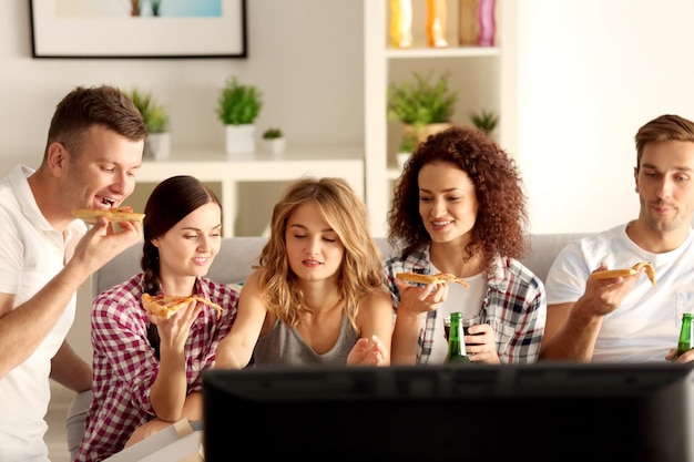 Photo friends eating pizza and watching tv at home party