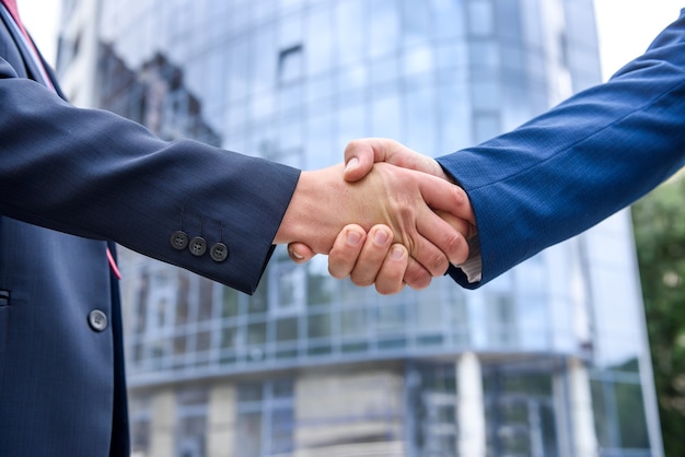 Friends in elegant business suits handshaking outdoors