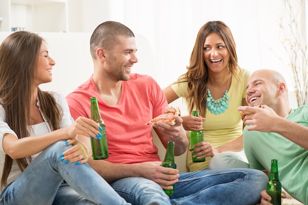 Amici che si divertono a mangiare la pizza e bere una birra insieme a casa.