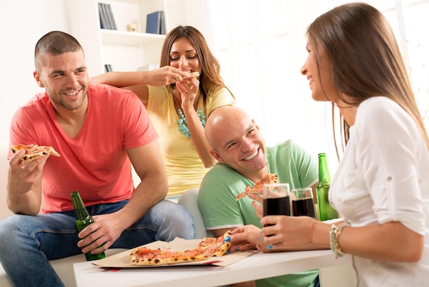 Amici che si divertono a mangiare la pizza e bere una birra insieme a casa.