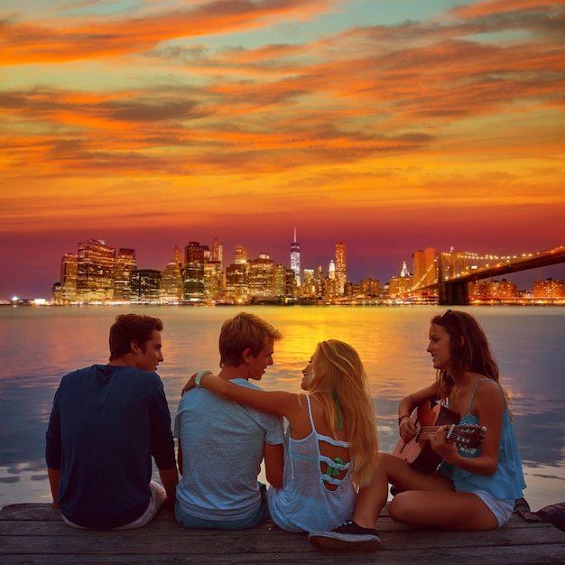 Friends group playing guitar in sunset pier at dusk