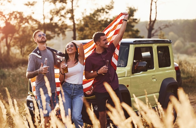 Friends have nice weekend outdoors near theirs green car with USA flag