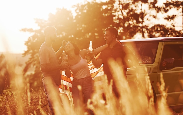 Friends have nice weekend outdoors near theirs green car with USA flag