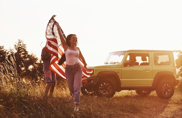 Friends have nice weekend outdoors near theirs green car with USA flag