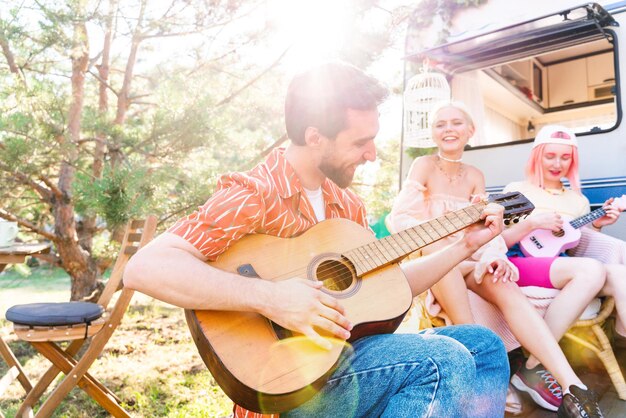 Friends have a picnic with a camper and play with guitar