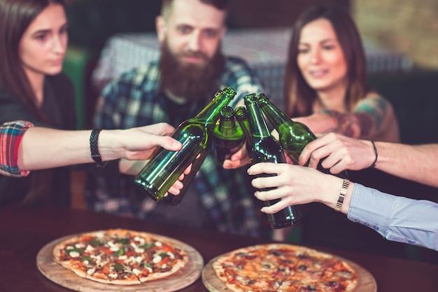 Friends having a drinks in a bar, They are sitting at a wooden table with beers and pizza.