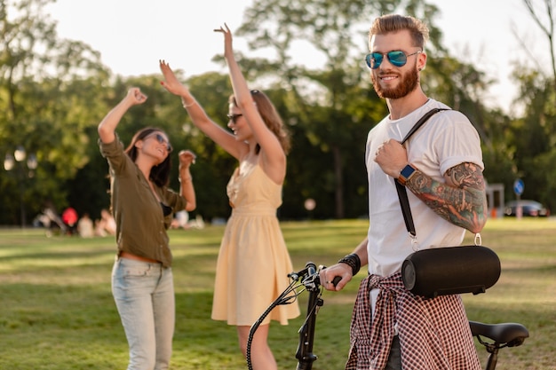 friends having fun together in park smiling listening to music on wireless speaker