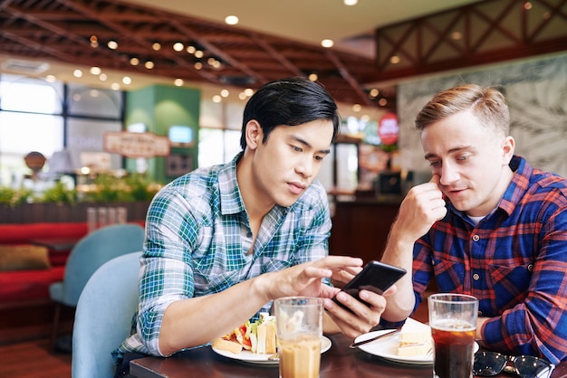 Friends having lunch in cafe and going through dating app on smartphone swiping left or right