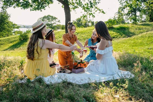 写真 樹木の近くの公園で毛布の上に座っている若い女性のグループが田舎でピクニックをしている友達