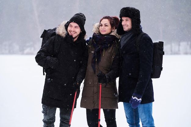 Friends hiking in the cold snowy forest stand in a hug and look at the camera.