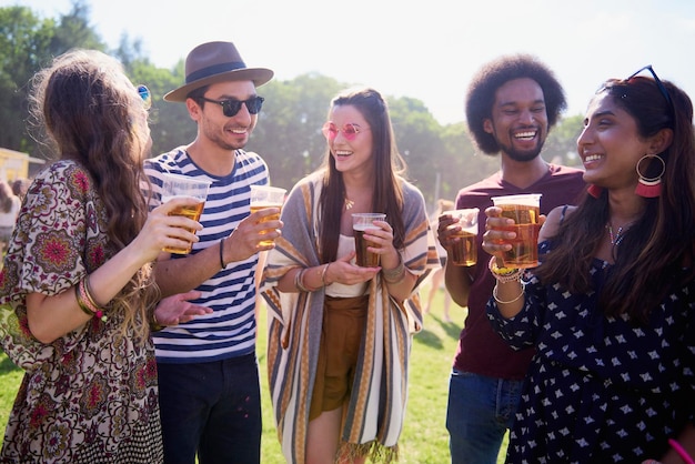 Friends holding beer in glasses while standing on grass