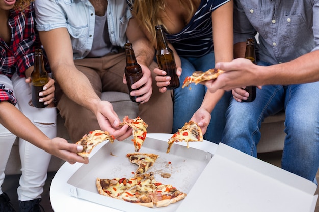 Photo friends holding beer while eating pizza at home