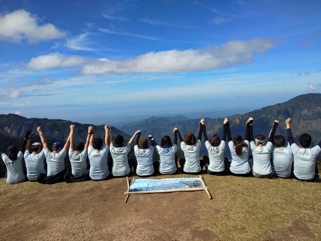 Foto amici che si tengono per mano mentre sono seduti contro le montagne.